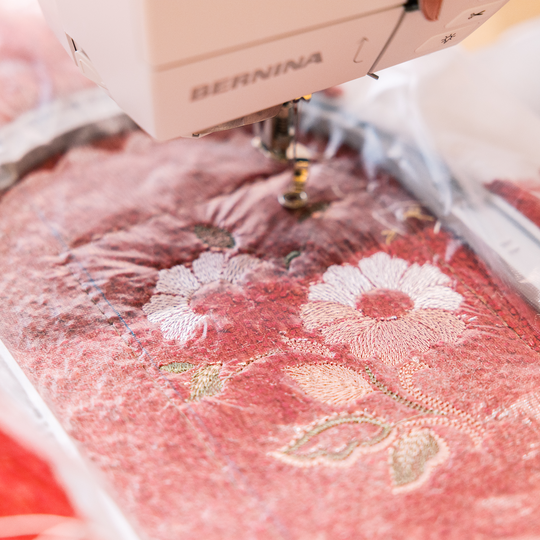 BERNINA Stickmaschine in Aktion beim Besticken eines rosafarbenen Stoffes mit floralen Mustern und feinen Quiltlinien im Detailansicht image number